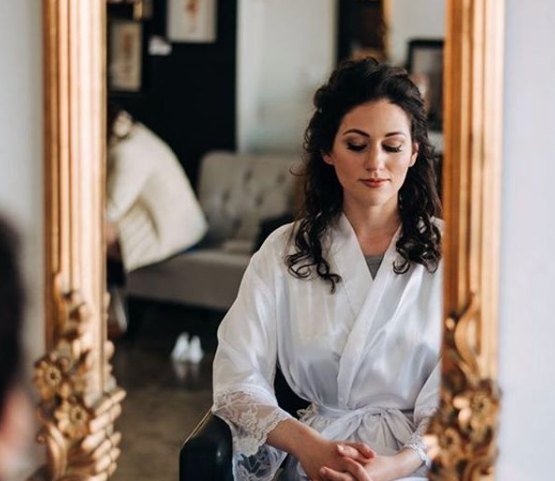 Bride with soft curls getting ready by a gold mirror